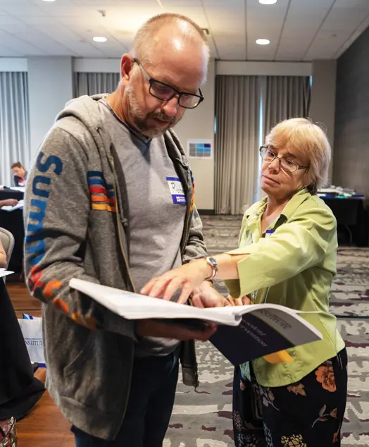 A woman pointing out something in a CPI workbook to a man.